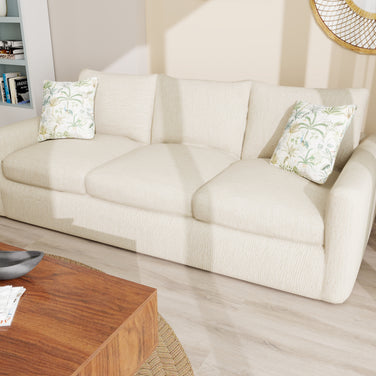 Clayhaven beige 3-seater fabric sofa with curved arms and three seat cushions, styled with botanical pillows in a modern living room.